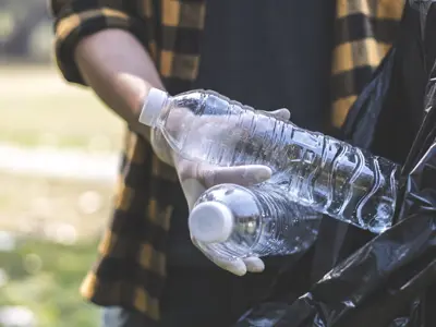 person throwing empty water bottles into a black garbage bag